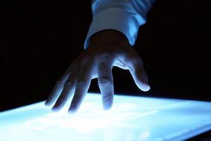 Human hand interacting with a glowing touchscreen in a dark environment, showcasing technology photo