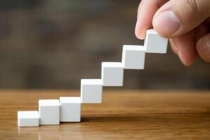 Hand arranging small white cubes into a staircase pattern on a wooden surface photo
