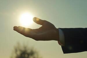 Hand reaching towards a bright sun during sunset, symbolizing hope and aspiration photo