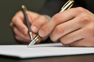 Hands of a business professional signing a document with a fountain pen on a desk photo