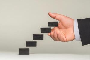 Hand in a suit placing black blocks in a staggered arrangement on a flat surface photo