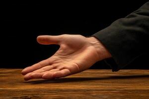 Outstretched hand reaching for assistance on a wooden table against a dark background photo