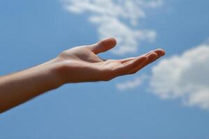 Outstretched hand reaching towards a bright blue sky with fluffy white clouds overhead photo