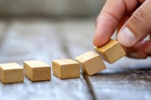 Hand placing wooden blocks in a line on a rustic wooden table, symbolizing growth and strategy photo