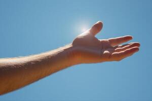 Outstretched hand reaching towards the bright sun against a clear blue sky, symbolizing hope photo