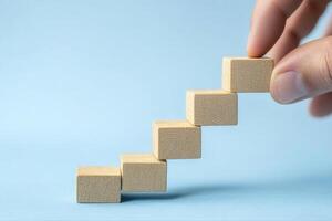 Hand placing wooden blocks in a step formation on a blue background, symbolizing growth photo