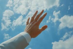 Reaching for the Sky A Businessman Extends Hand Towards Bright Blue Sky with Clouds photo