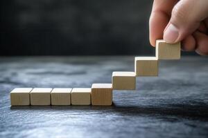 Hand arranging wooden blocks into a staircase pattern on a dark textured surface photo