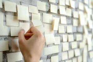 Hand placing a sticky note on a textured wall filled with blank notes, symbolizing ideas photo