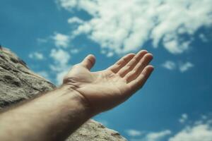 Outstretched hand reaching towards a bright blue sky with fluffy clouds in the background photo