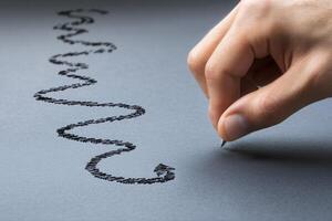 Hand drawing a wavy line on dark paper with a pencil, showcasing artistic expression photo