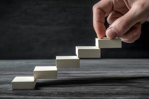 Hand placing wooden blocks to create a staircase, symbolizing growth and progress photo