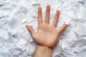 Hand reaching out amidst crumpled paper, symbolizing struggle or frustration in work photo