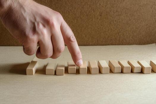 Hand poised to topple wooden blocks in a sequential arrangement on a neutral backdrop photo
