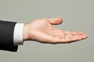 Open hand gesture in a business suit against a neutral background, symbolizing offering photo