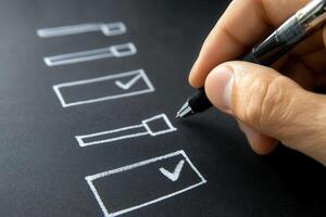 Hand holding a pen marking checkboxes on a black background, symbolizing task completion photo