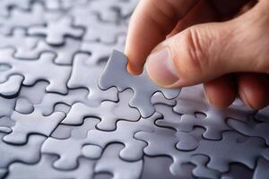 Hand placing a puzzle piece onto a nearly completed gray puzzle on a table photo