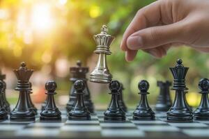 Hand moving a silver king piece in a chess game on an outdoor board during sunset photo