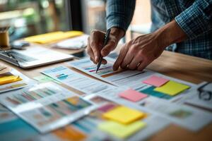 Person analyzing colorful charts and graphs at a desk with sticky notes and laptop photo