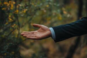 Man in a suit extending his hand in a natural setting, inviting connection amidst greenery photo