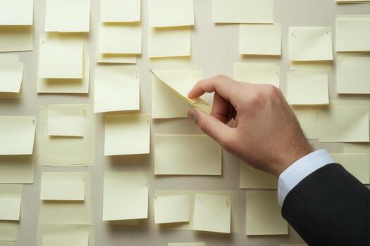 Hand removing a sticky note from a wall covered with yellow notes in a modern office setting photo