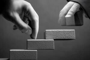 Two hands placing textured blocks on a staircase, symbolizing progress and teamwork photo