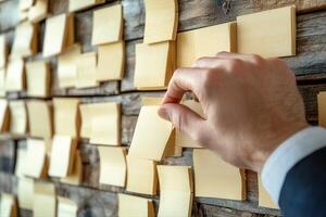 Hand removing a sticky note from a wooden wall covered in blank notes, ideal for brainstorming photo