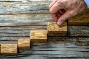 Hand placing wooden blocks in a step formation on a rustic wooden surface, symbolizing progress photo