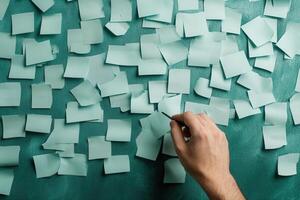 Hand writing on a teal surface covered with scattered sticky notes in a creative workspace photo