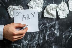 Hand holding a pen writing 'ALLY' on a notepad with crumpled paper in the background photo