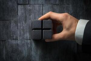 Hand holding four interconnected dark cubes against a textured gray wall background photo