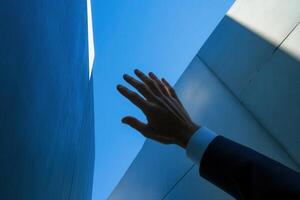 Hand reaching towards the sky between two modern architectural structures in a bright blue setting photo