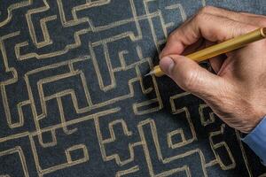 Hand drawing intricate maze patterns on black surface with yellow pen, creative process photo
