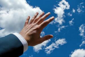Reaching for the Sky A Businessman Extends His Hand Towards a Bright Blue Sky with Clouds photo
