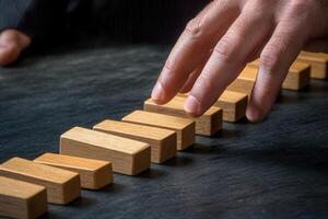 Hand poised to topple wooden blocks in a strategic business decision-making scenario photo