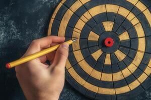 Hand holding a pencil poised to mark a target on a dartboard with a textured background photo