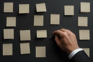 Hand placing a pen on blank sticky notes arranged on a dark surface, ideal for brainstorming photo