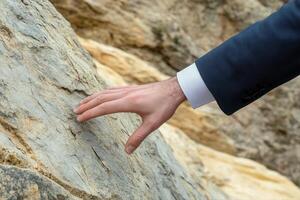 Man in a suit gently touching a rocky surface, exploring nature's textures outdoors photo