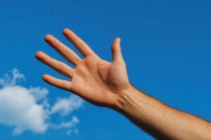 Hand reaching towards a clear blue sky with fluffy clouds in the background photo