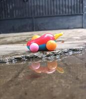A Colorful Toy Car Reflected in a Puddle on a Concrete Surface. photo