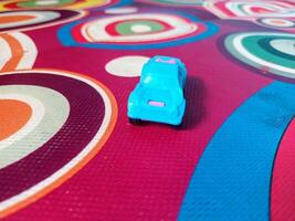 A Tiny Blue and Pink Toy Car on a Multicolored Circular Patterned Mat. photo