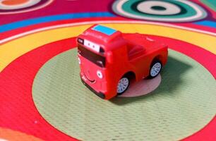 A Small Red Toy Bus with a Smiling Face on a Colorful Circular Patterned Mat. photo