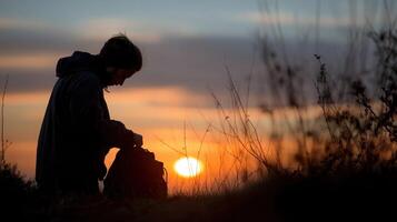 A silhouette of a person packing a bag in the early dusk with a sense of anticipation for the days adventures ahead as the sun sets in the background photo