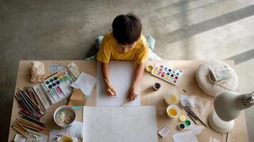 A boy sketching ideas on a large sheet of paper spread out on the floor with various art supplies and a nearby lamp illuminating his creative process photo