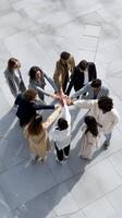 Diverse group joining hands in a circle on light-colored pavement. Teamwork, unity, collaboration, and support are evident photo