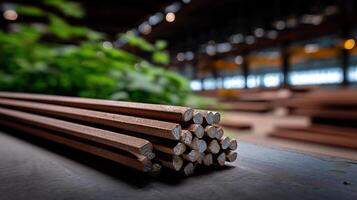 Stacked metal rods in a factory setting. Close-up view of grouped, reddish-brown metal bars. Blurred background shows more metal parts and greenery photo