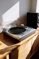 Record player on light wooden cabinet, sunlight streams in photo