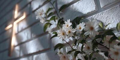 Illuminated cross on a white brick wall adorned with white flowers photo