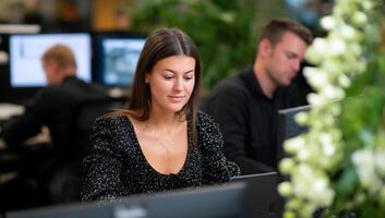 Focused woman working at a computer in a modern office, colleagues in background photo