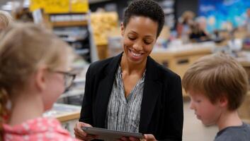 Teacher interacting with children in a store, likely showing them something on a tablet. Children and teacher engaging in learning activity photo